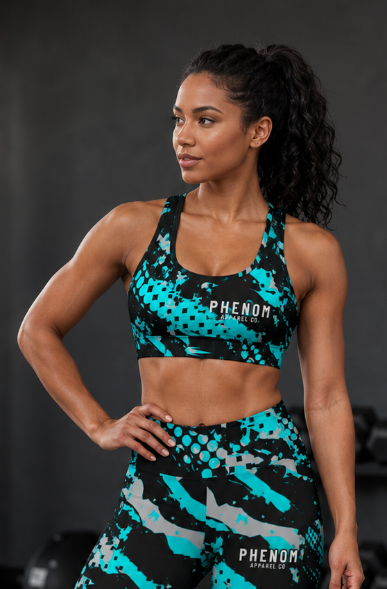 A woman modeling a matching athletic set in a gym, featuring a black sports bra and high-waisted leggings with a teal and gray pixelated camouflage pattern. The brand name 'PHENOM' is printed on both pieces.