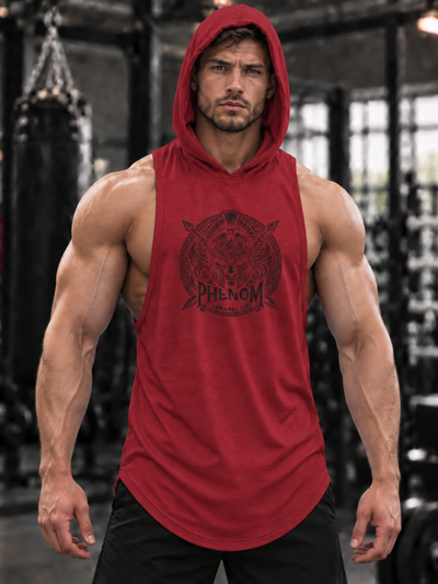 A muscular man wearing a red sleeveless hooded tank top with 'PHENOM FORGE' printed in black across the chest, standing in a gym with a blurred background.