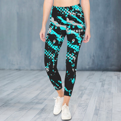 A model from the waist down wearing high-waisted athletic leggings with a black, teal, and gray shark-scale pattern, paired with white sneakers, set against a gray studio backdrop.