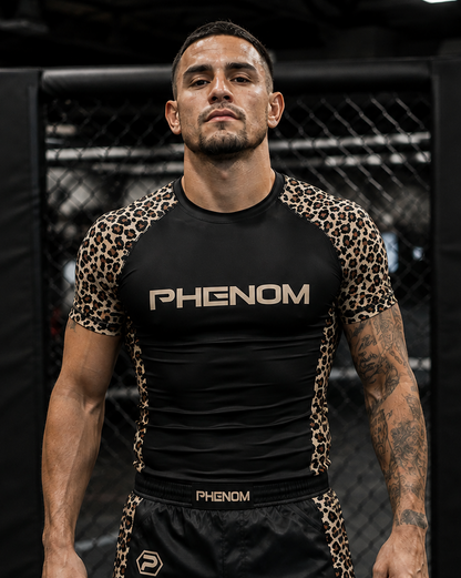 A man wearing a black and leopard-print Phenom rash guard and matching black rash guard shorts with leopard-print side panels, standing in an MMA ring.