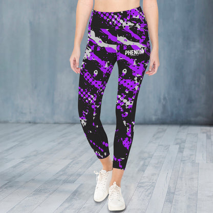 A person modeling high-waisted leggings with a black, purple, and gray camouflage pattern, featuring the word 'PHENOM' on the upper right thigh, paired with white sneakers against a gray studio backdrop.